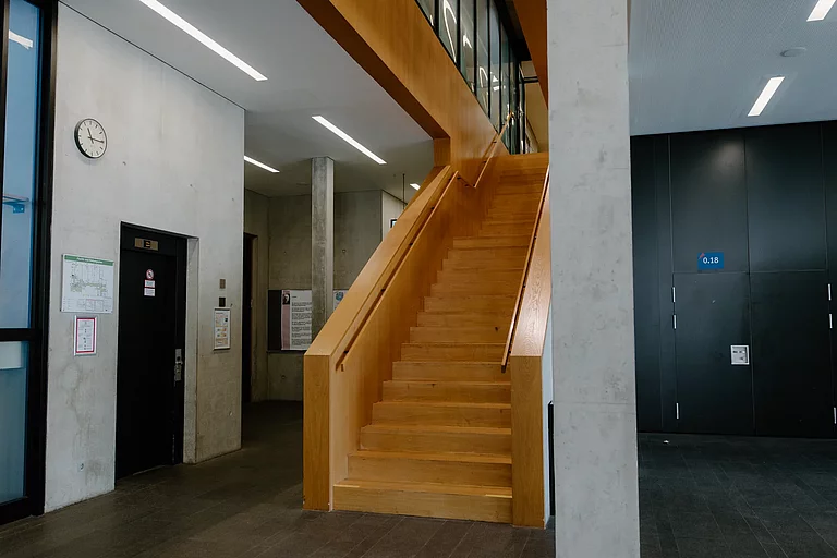 Das Foto zeigt eine große Holztreppe, die im G-Gebäude in den ersten Stock führt und direkt am Schülersekretariat endet.