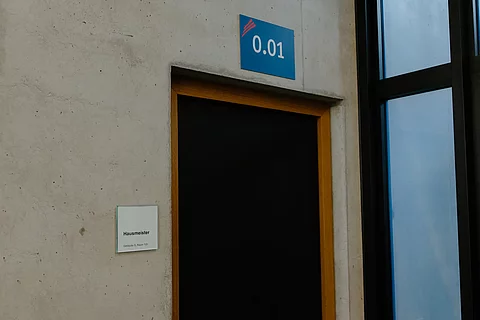 Das Foto zeigt die Tür zum Hausmeisterbüro im G-Gebäude der Schule. Die Raumnummer ist 0.01.