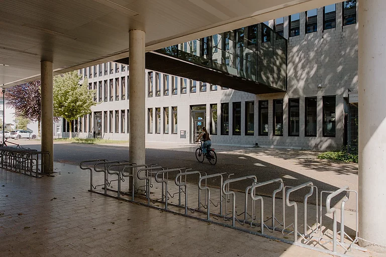 Das Foto zeigt einen Fahrradständer, der sich zwischen dem G-Gebäude und dem F-Gebäude befindet. Er ist direkt neben dem Büro des Hausmeisters.