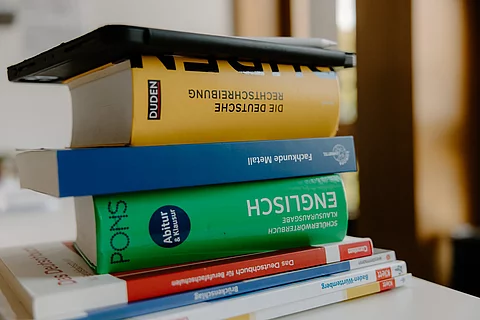 Das Foto zeigt einen Stapel verschiedener Schulbücher und ein Tablet ganz oben auf dem Stapel.