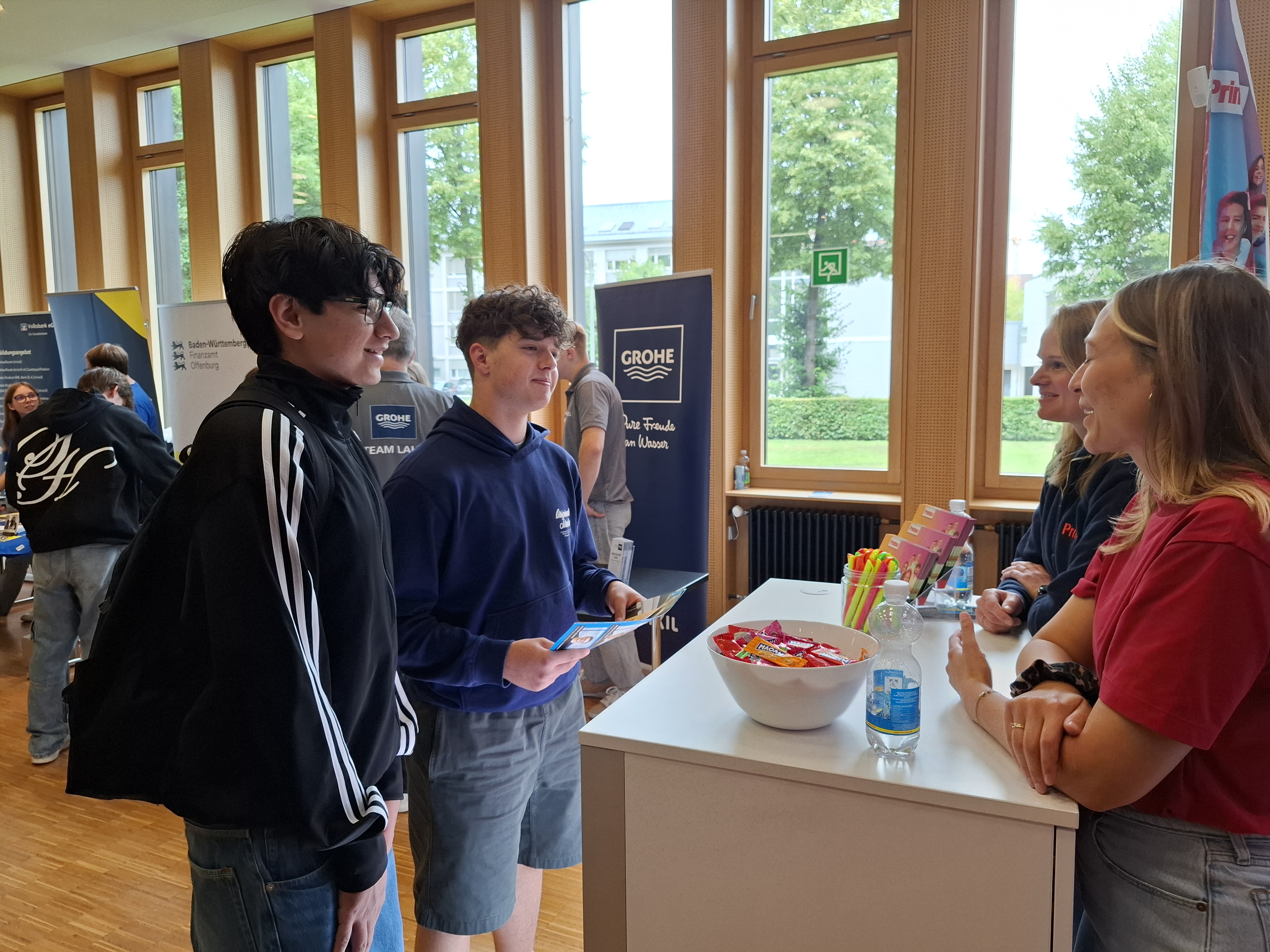 Das Foto zeigt zwei Schüler, die vor einem Infostand der Berufsinfomesse in der Schule stehen.